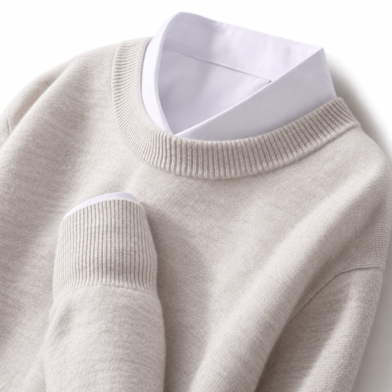 A close-up of a light beige knit sweater layered over a white collared shirt, showing the ribbed crew neck and sleeve cuffs.