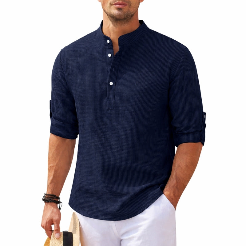 Man wearing a navy blue textured shirt with white pants on a white background