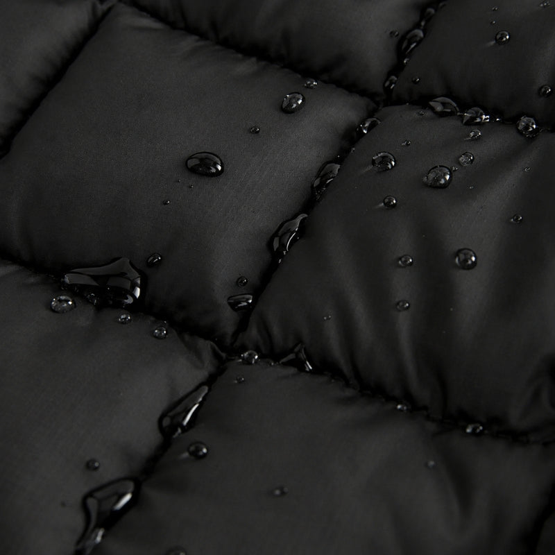 Close-up of a black quilted padded fabric with water droplets beading on the surface, showing the material texture and waterproof finish.