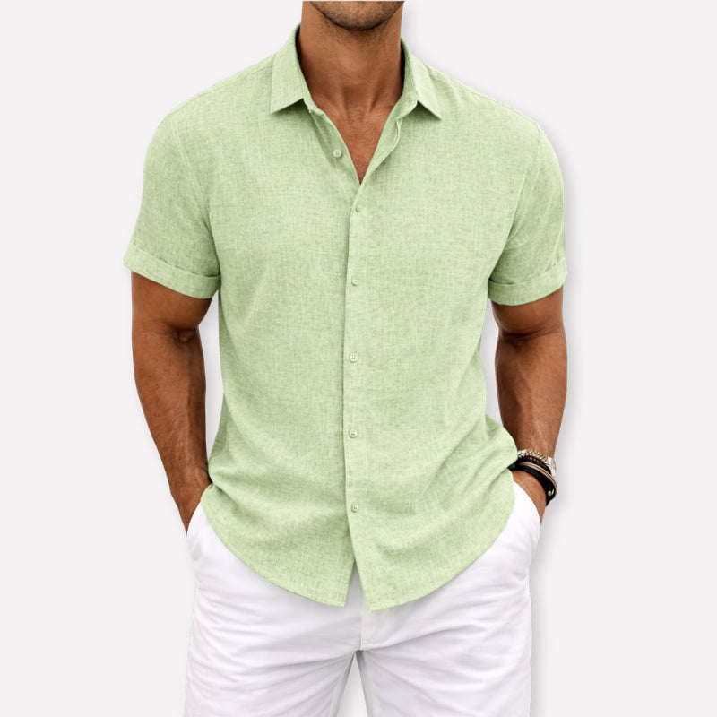 Man wearing a light green short-sleeve shirt and white pants against a white background