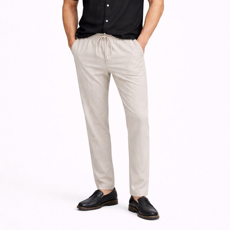 Person wearing beige linen pants and black shoes on a white background