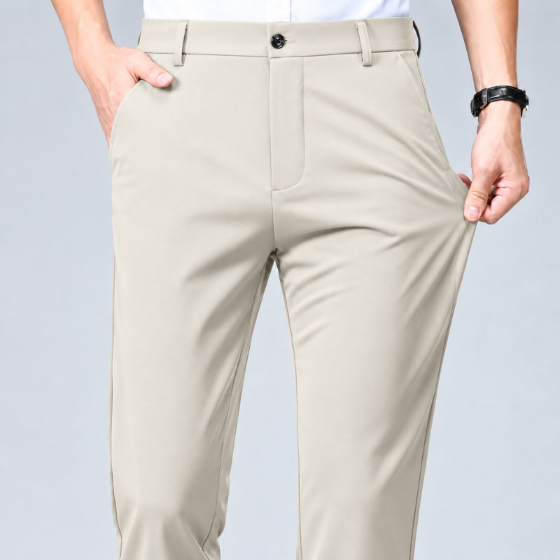 A close-up of a person wearing light beige dress pants, showing the front waistband, button, pockets, and legs against a plain light gray studio background.