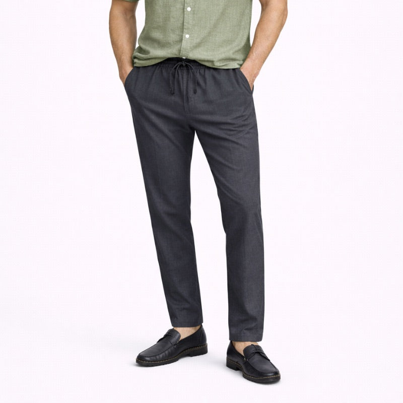 Person wearing gray linen pants and black shoes on a white background