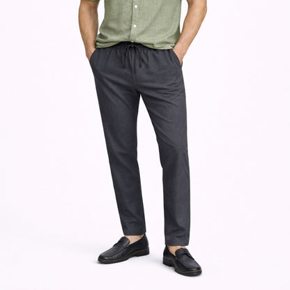 Person wearing gray linen pants and black shoes on a white background