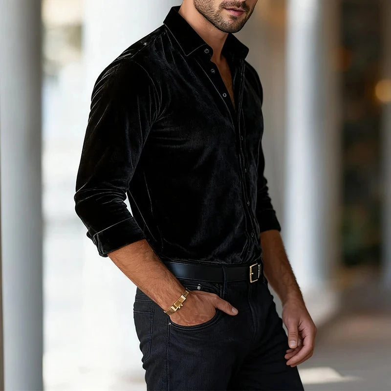 Man wearing a black velvet shirt and dark jeans with a blurred background