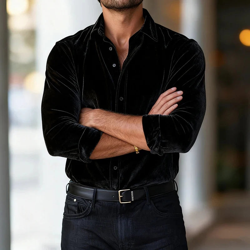 Man wearing a black velvet shirt with arms crossed against a blurred background