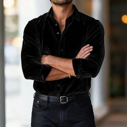 Man wearing a black velvet shirt with arms crossed against a blurred background