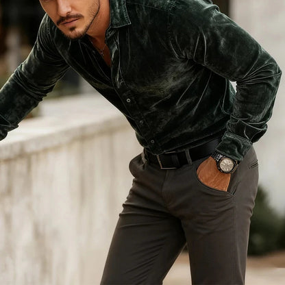Man wearing a dark green velvet shirt and black pants with a blurred background
