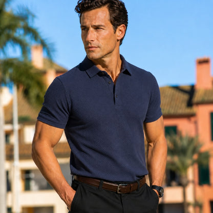 Man wearing a navy blue polo shirt with a blurred background of buildings and palm trees.
