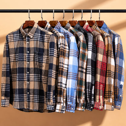 A group of men's long-sleeve plaid button-up shirts hanging on wooden hangers from a black rod against a warm beige background. The shirts feature various plaid patterns in blue, brown, red, green, black, and white.