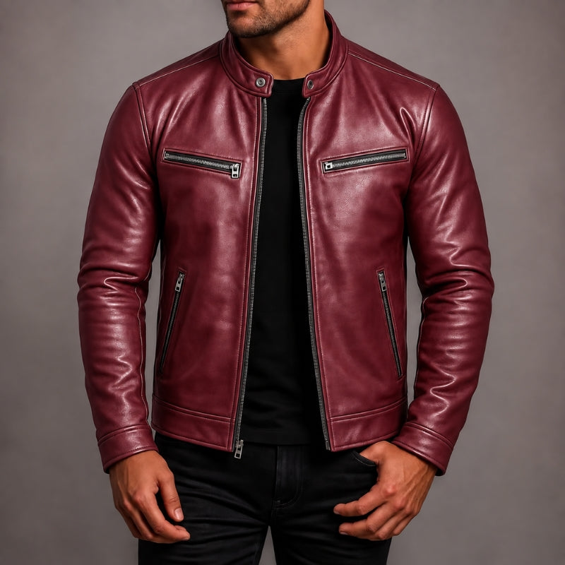 A man wearing a burgundy leather motorcycle jacket with silver zippers over a black shirt and black pants, photographed against a neutral gray studio background.