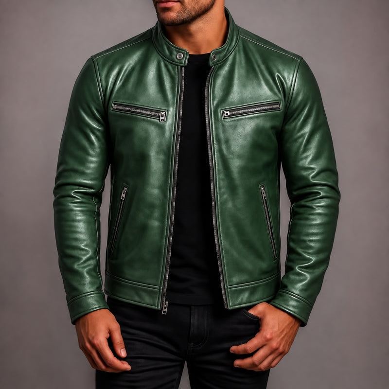 A man wearing a dark green leather jacket with silver zippers over a black shirt and black pants, photographed against a plain gray studio background.