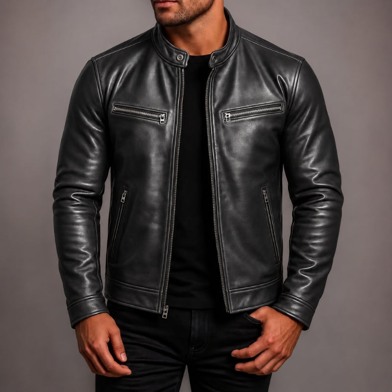 A man wearing a black leather jacket with silver zippers over a black shirt, shown from the chin down against a plain gray studio background.