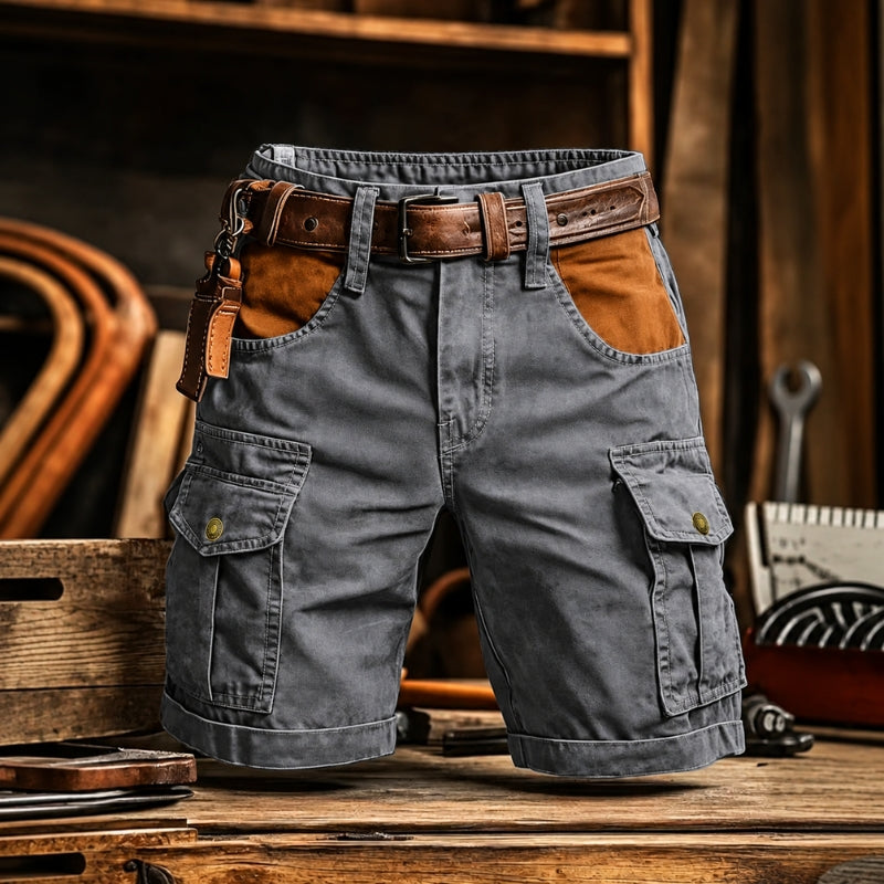 Gray cargo shorts with brown leather accents, including a matching belt, belt loops, and a leather key fob, displayed on a rustic wooden table.