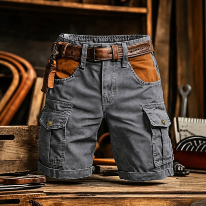 Gray cargo shorts with brown leather accents, including a matching belt, belt loops, and a leather key fob, displayed on a rustic wooden table.