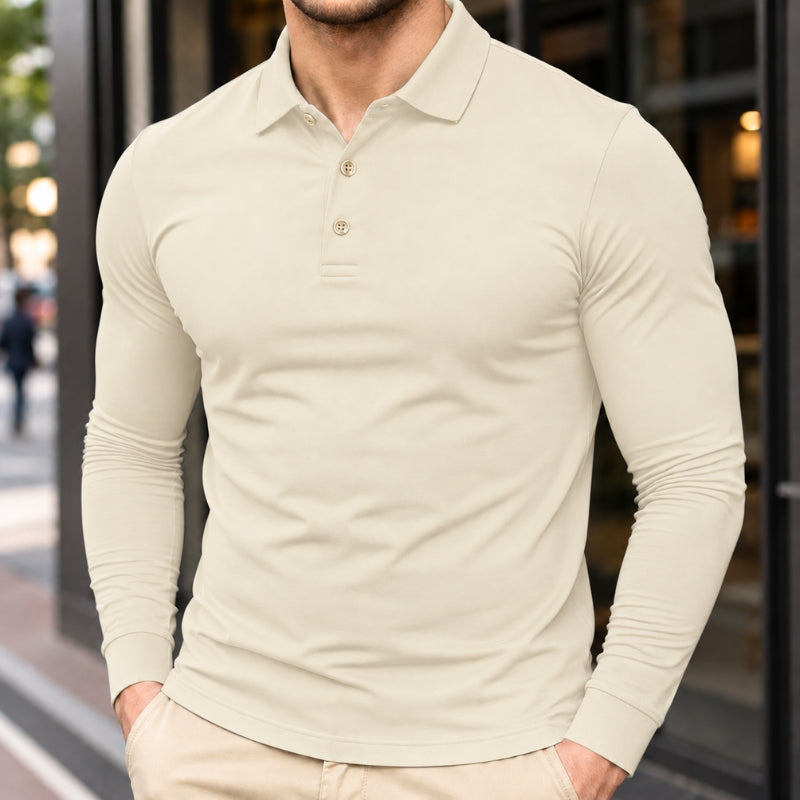 A man wearing a fitted long-sleeve polo shirt in a light cream or off-white color, standing outdoors in front of a modern building with dark-framed windows.