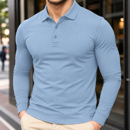 A man wearing a light blue long-sleeve polo shirt with a buttoned collar, paired with beige pants, standing in front of a blurred storefront background.
