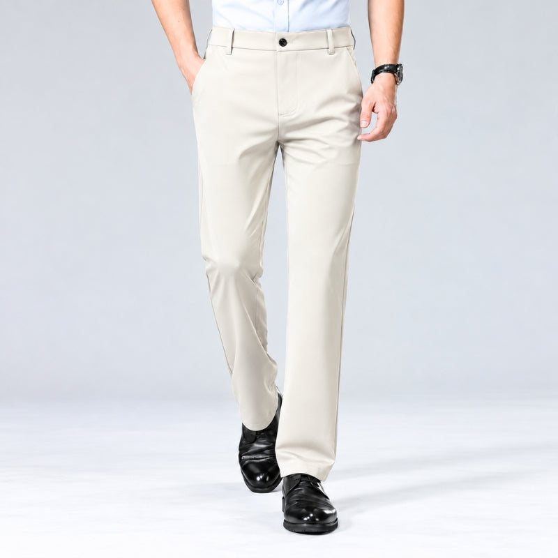 A man wearing light beige dress pants with a white shirt and black dress shoes, shown from the waist down against a light gray studio background.