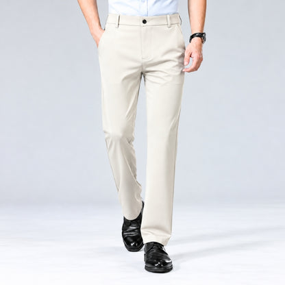 A man wearing light beige dress pants with a white shirt and black dress shoes, shown from the waist down against a light gray studio background.