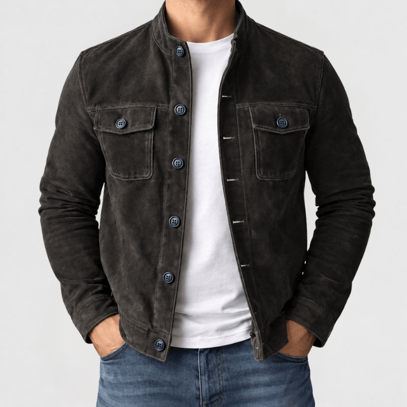 A man wearing a dark brown suede jacket over a white t-shirt and blue jeans, shown from the neck down against a light gray background.