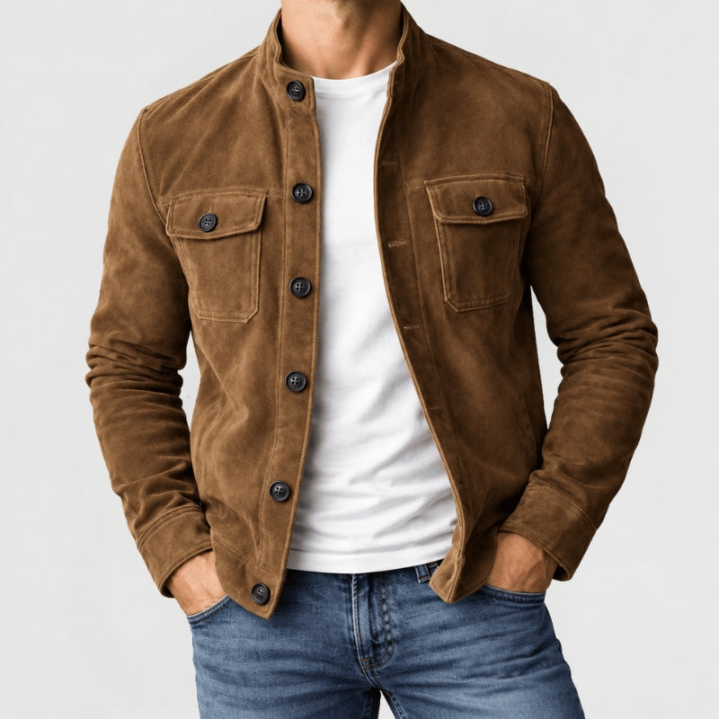 A man wearing a brown suede jacket over a white t-shirt and blue jeans, shown from the neck down against a light gray background.