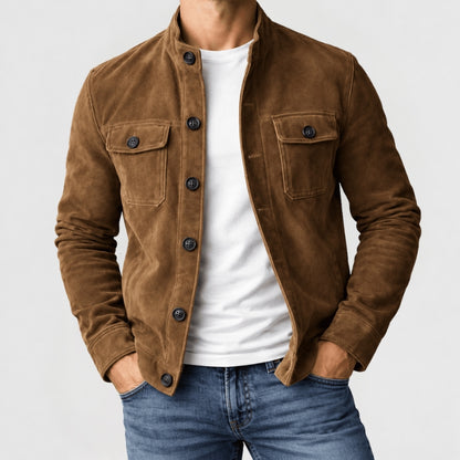 A man wearing a brown suede jacket over a white t-shirt and blue jeans, shown from the neck down against a light gray background.