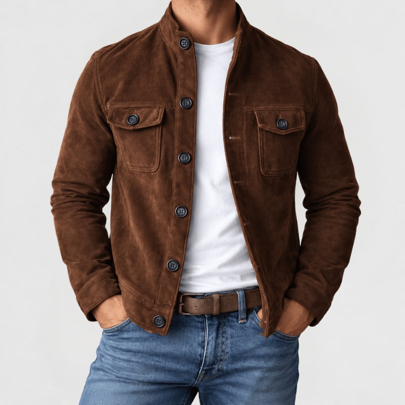 A man wearing a brown suede jacket over a white t-shirt and blue jeans, standing against a light gray background.