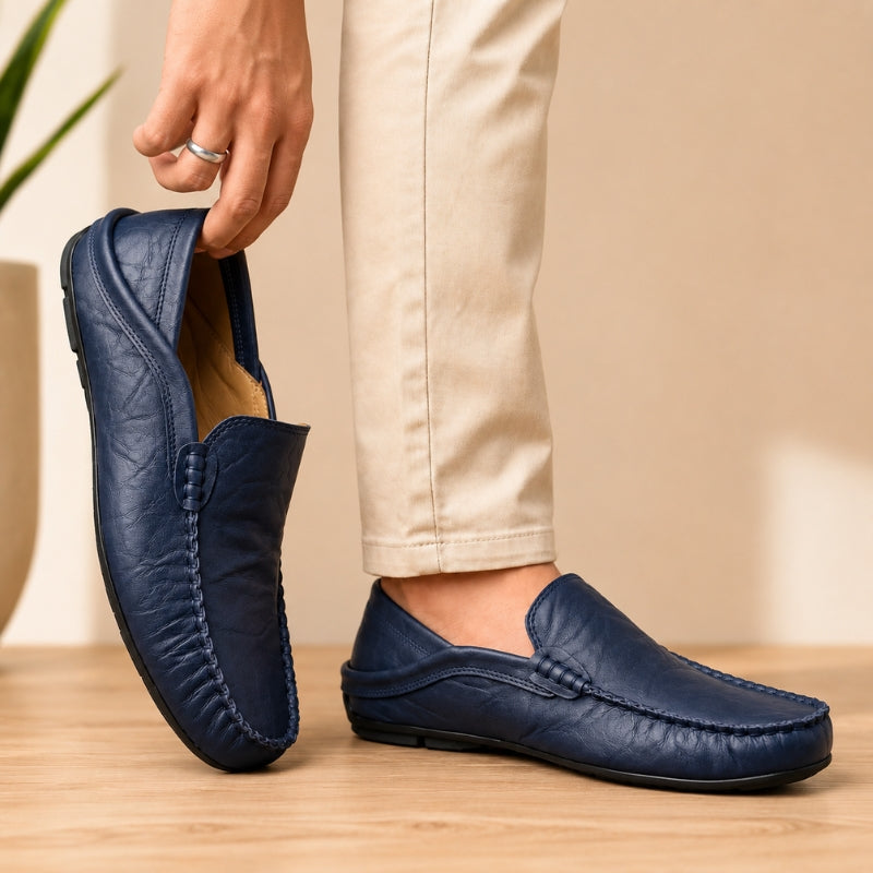 Navy blue loafers worn with beige pants on a wooden floor.