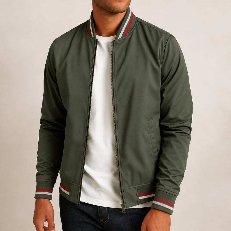 A man wearing an olive green zip-up bomber jacket with red and white striped ribbed collar, cuffs, and hem, layered over a white t-shirt and dark jeans.