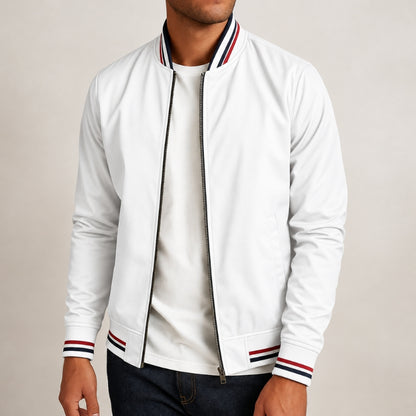 A man wearing a white zip-up bomber jacket with red and navy striped ribbed collar, cuffs, and hem, paired with a white t-shirt and dark jeans, against a plain light beige background.