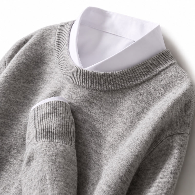 A close-up of a light gray knit sweater layered over a white collared shirt, shown against a plain white background.