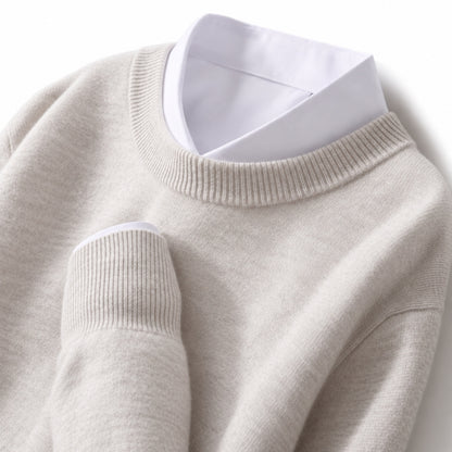 A close-up of a light beige knit sweater layered over a white collared shirt, showing the ribbed crew neck and sleeve cuffs.