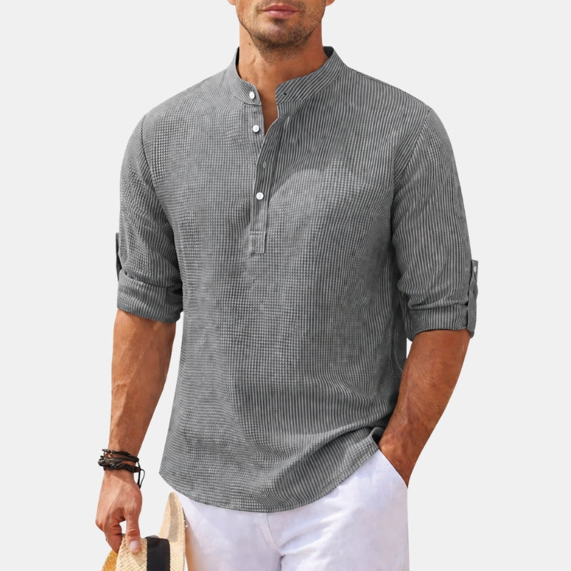 Man wearing a gray patterned shirt with rolled-up sleeves on a light background