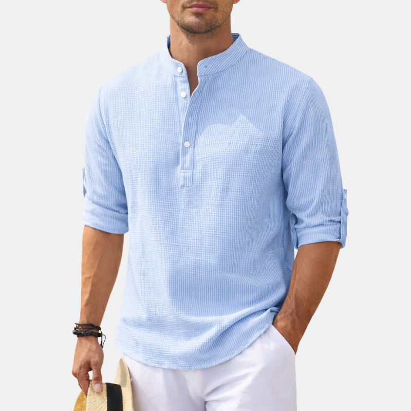 Man wearing a light blue textured shirt with rolled-up sleeves on a white background