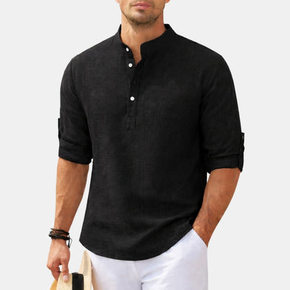 Man wearing a black textured shirt with white pants on a light gray background