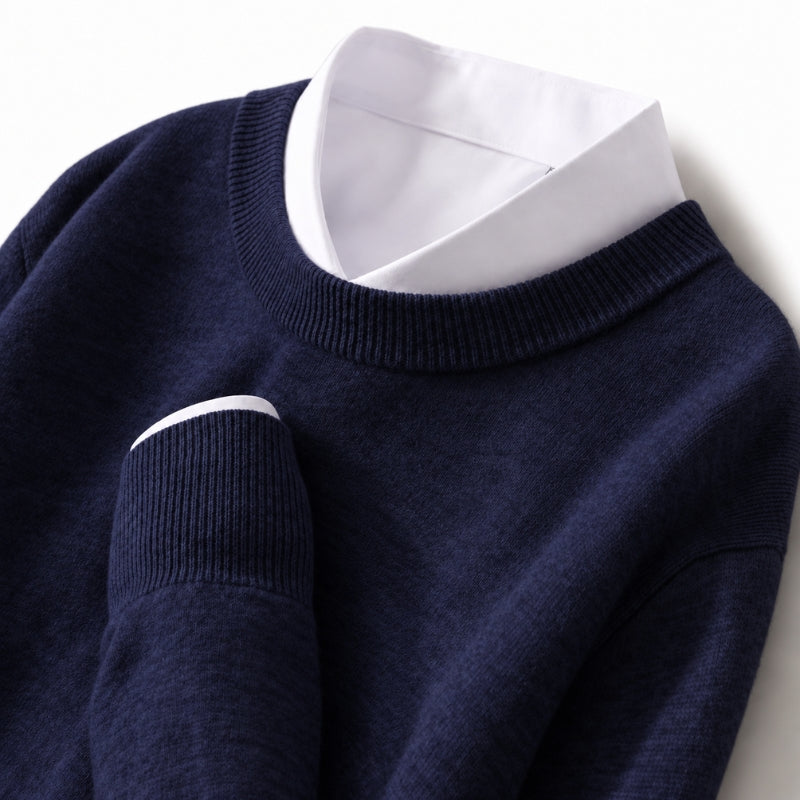 A close-up of a navy blue knit sweater layered over a white collared shirt, shown against a clean white background.