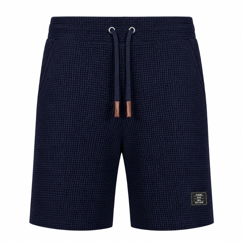 A pair of men's navy blue textured shorts with a matching drawstring and a small brand patch on the lower left leg, shown against a plain white background.