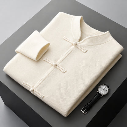 A folded cream-colored knit traditional Chinese-style sweater with a mock neck and button closures, displayed on a dark gray block alongside a wristwatch.