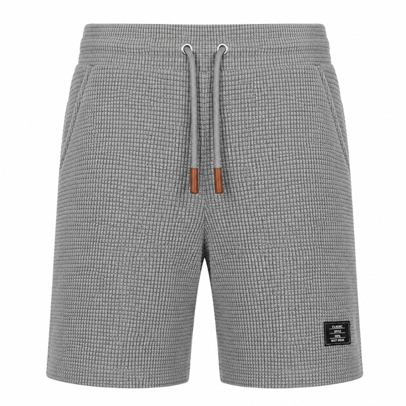 Gray textured knit shorts with a drawstring waist and a small black brand patch on the lower right leg, shown against a plain white background.