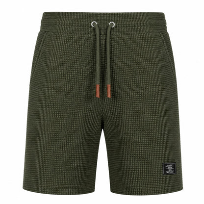 Olive green textured knit shorts with a matching drawstring and a small black brand patch on the lower left leg, shown against a plain white background.