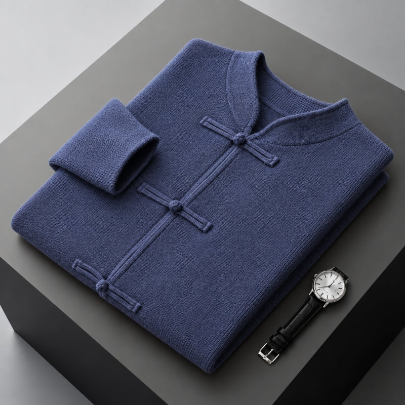 A folded navy blue knit sweater with a mandarin collar and button closures, displayed on a dark gray pedestal next to a wristwatch.