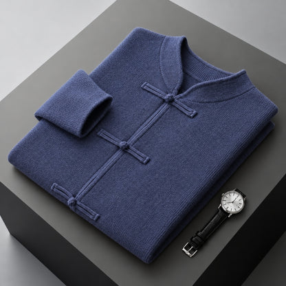 A folded navy blue knit sweater with a mandarin collar and button closures, displayed on a dark gray pedestal next to a wristwatch.
