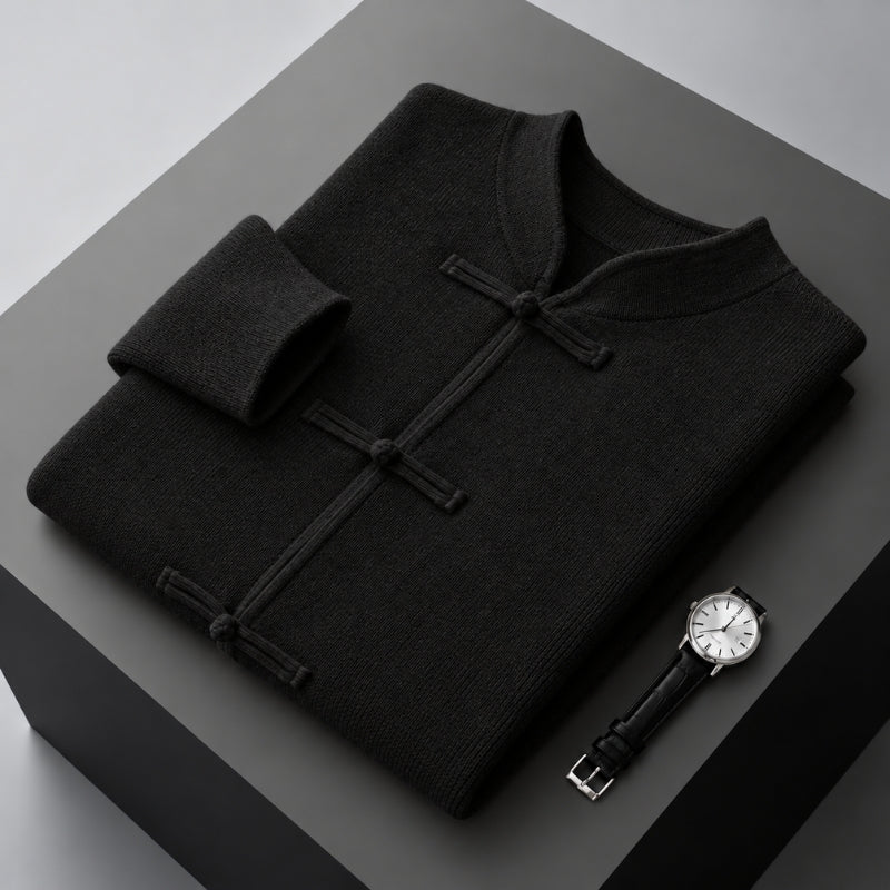 A folded black knit sweater with a mandarin collar and dark button closures, displayed on a dark gray geometric surface next to a wristwatch.