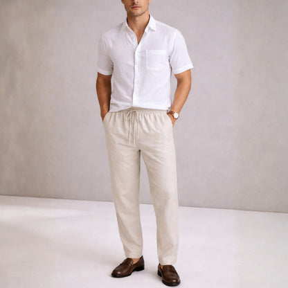Man wearing a white shirt and beige pants against a plain background