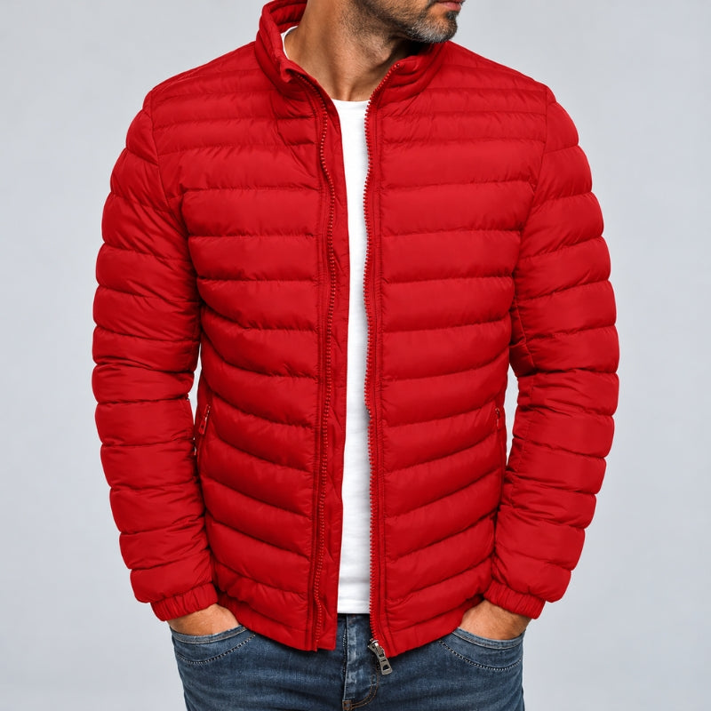 A man wearing a bright red puffer jacket over a white t-shirt and blue jeans, shown from the chin down against a light gray studio background.