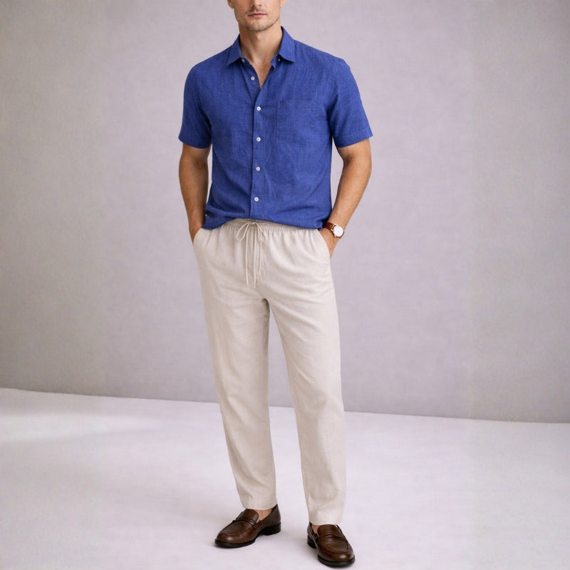 Man wearing a blue shirt and beige pants against a plain background
