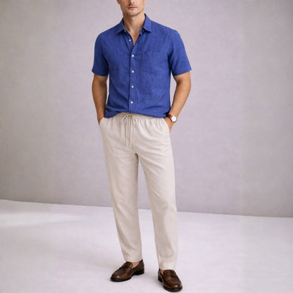 Man wearing a blue shirt and beige pants against a plain background