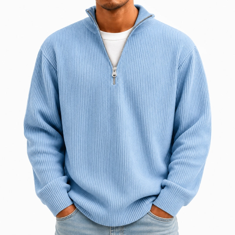 A man wearing a light blue ribbed quarter-zip pullover sweater over a white t-shirt and light-wash jeans, shown from the neck down against a plain white background.