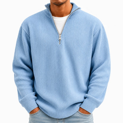 A man wearing a light blue ribbed quarter-zip pullover sweater over a white t-shirt and light-wash jeans, shown from the neck down against a plain white background.