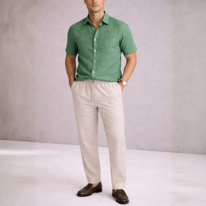 Man wearing a green shirt and beige pants against a plain background
